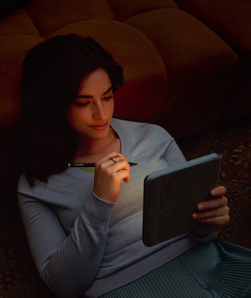 Una mujer reclinada en un sofá, iluminada por la suave luz de un eReader Kobo Libra Colour que sostiene, junto con un Kobo Stylus 2.