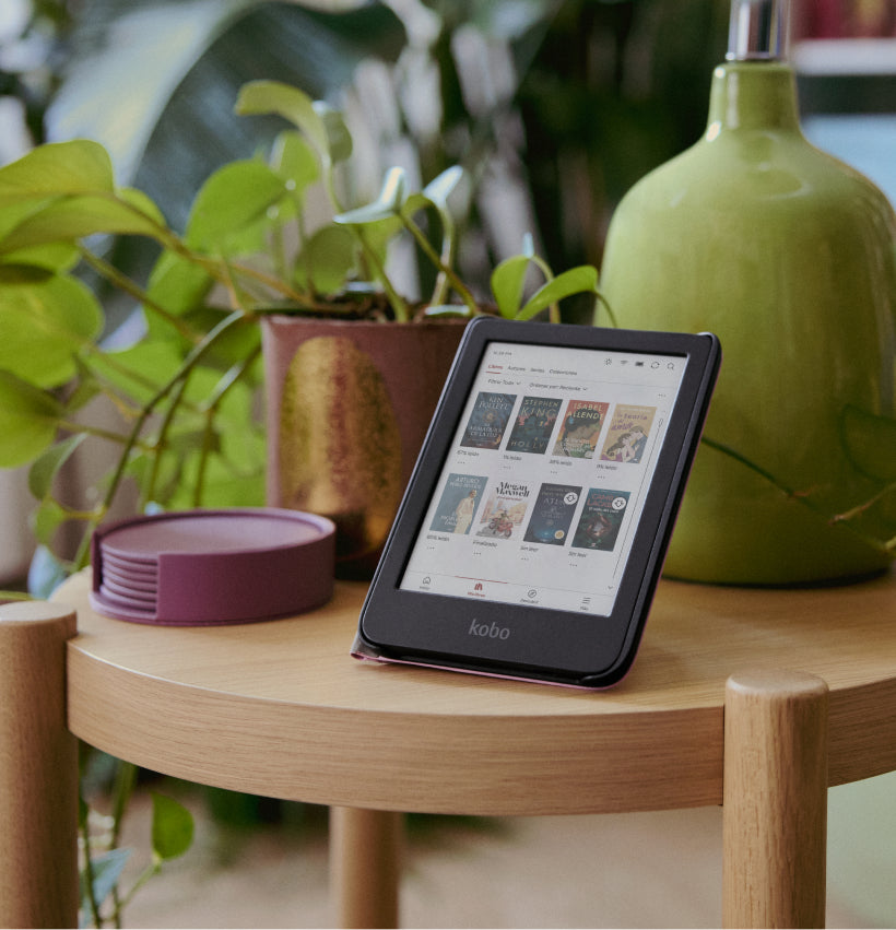 Un eReader Kobo Clara Colour en su soporte SleepCover, colocado sobre una mesa de madera junto a una maceta y una lámpara.