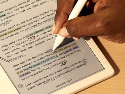 Se muestra una mano usando el Kobo Stylus 2 para escribir directamente en un eBook en un eReader Kobo Libra Colour sobre una superficie plana. En la página, vemos anotaciones y resaltados coloridos.