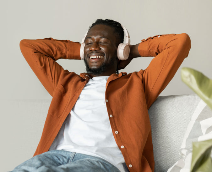 Un hombre sonriente con auriculares, recostado con los ojos cerrados.